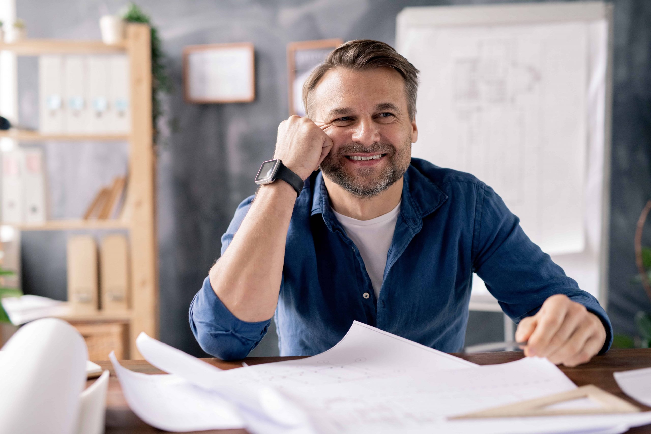 Man in blue shirt, hand near face looking at plans.